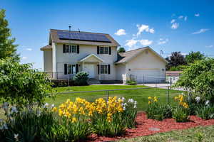 Colonial inspired home with roof mounted solar panels, a garage, roof with shingles, and driveway
