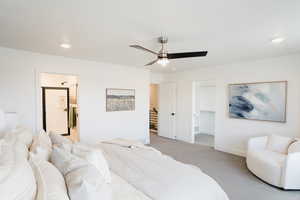 Bedroom with a walk in closet, light carpet, baseboards, a ceiling fan, and ensuite bath