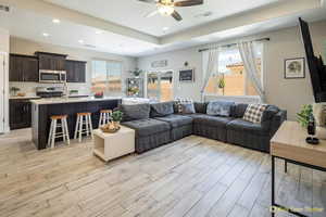 Living room featuring light wood finished floors, ceiling fan, recessed lighting, and a raised ceiling