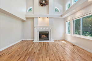 Unfurnished living room featuring a high ceiling, a fireplace, plenty of natural light, wood finished floors, and baseboards