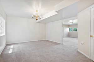 Unfurnished room featuring light colored carpet, a chandelier, and baseboards