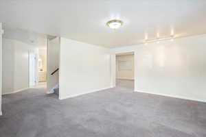 Unfurnished room featuring carpet flooring, baseboards, stairway, and track lighting