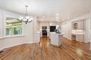 Kitchen featuring appliances with stainless steel finishes, a kitchen island, tile counters, light wood finished floors, and tasteful backsplash