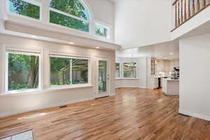 Unfurnished living room featuring a towering ceiling, a chandelier, light wood-style floors, baseboards, and a sink