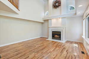 Unfurnished living room with a tiled fireplace, a high ceiling, wood finished floors, healthy amount of natural light, and baseboards