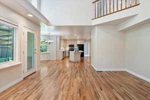 Unfurnished living room with a towering ceiling, a chandelier, light wood-type flooring, baseboards, and recessed lighting