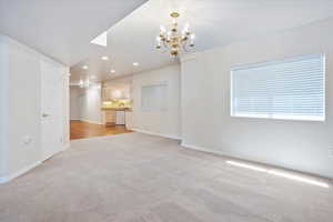 Unfurnished living room with a chandelier, light colored carpet, baseboards, and recessed lighting