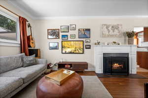 Living room featuring dark wood-style floors, crown molding, a warm lit fireplace, and baseboards