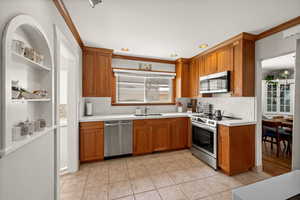 Kitchen featuring appliances with stainless steel finishes, a sink, light countertops, brown cabinetry, and recessed lighting