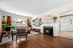 Living room with a fireplace with flush hearth, ornamental molding, and wood finished floors