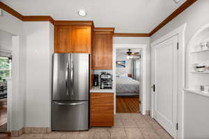 Kitchen with freestanding refrigerator, ornamental molding, brown cabinetry, light countertops, and ceiling fan