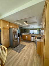 Kitchen featuring stainless steel appliances, a raised ceiling, light wood-style floors, a textured ceiling, and light countertops