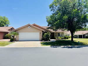 Ranch-style home featuring concrete driveway, stucco siding, a garage, a front lawn, and a tiled roof