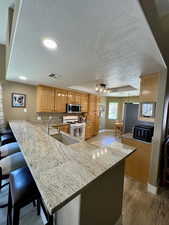 Kitchen featuring white gas range oven, stainless steel microwave, light wood-style flooring, a sink, and a textured ceiling