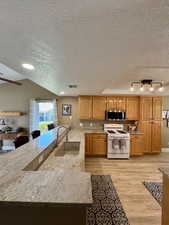 Kitchen featuring white range with gas cooktop, a sink, stainless steel microwave, a textured ceiling, and light wood-type flooring