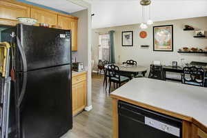 Kitchen featuring black appliances, light wood-style floors, light countertops, hanging light fixtures, and baseboards