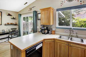Kitchen with dishwasher, a sink, vaulted ceiling, a peninsula, and light countertops
