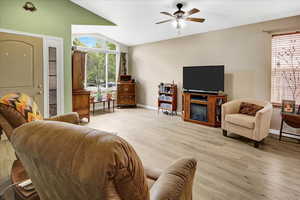 Living room featuring light wood finished floors, baseboards, ceiling fan, plenty of natural light, and lofted ceiling