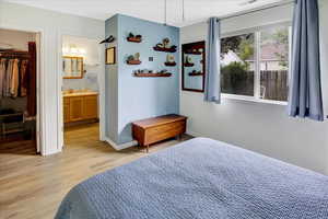 Bedroom featuring light wood finished floors, baseboards, a walk in closet, connected bathroom, and a sink