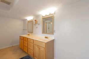 Bathroom with double vanity, a shower with shower door, baseboards, and tile patterned flooring
