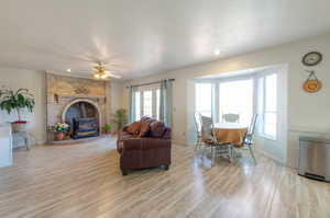 Living area featuring a wood stove, light wood-style floors, baseboards, ceiling fan, and a textured ceiling