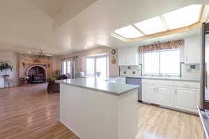 Kitchen with stainless steel dishwasher, a kitchen island, backsplash, open floor plan, and light wood-type flooring