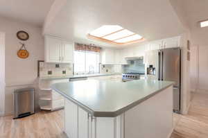 Kitchen with stainless steel appliances, white cabinetry, light wood-style flooring, decorative backsplash, and a textured ceiling