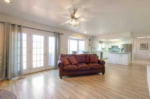 Living area featuring light wood finished floors, a textured ceiling, ceiling fan, and french doors