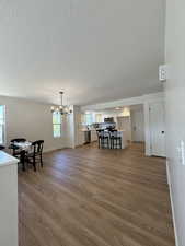 Living area with dark wood-type flooring, a textured ceiling, baseboards, and a chandelier