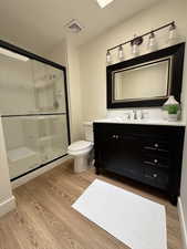 Full bathroom with wood finished floors, vanity, a shower stall, and toilet