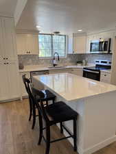 Kitchen with stainless steel appliances, a sink, white cabinetry, light wood-style flooring, and a textured ceiling