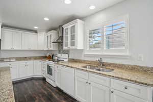 Kitchen with wall chimney range hood, white appliances, a sink, white cabinetry, and recessed lighting