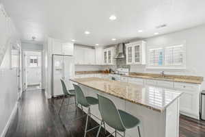 Kitchen featuring white appliances, wall chimney range hood, a kitchen breakfast bar, a sink, and white cabinetry
