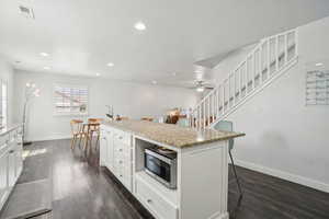 Kitchen featuring stainless steel microwave, a large kitchen breakfast bar, baseboards, dark wood-style floors, and white cabinetry