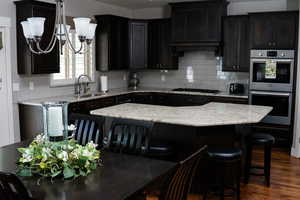 Kitchen with stainless steel double oven, a sink, black gas stovetop, tasteful backsplash, and a breakfast bar