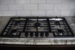 Kitchen view of stainless steel gas cooktop, tasteful backsplash, and light stone countertops