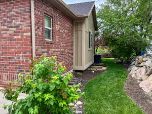 View of side of property featuring roof with shingles, central AC, brick siding, and a yard