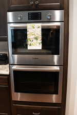 Kitchen view of dark brown cabinetry, double oven, light countertops, and tasteful backsplash