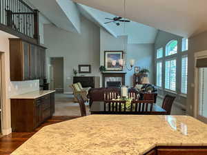 Dining room with high vaulted ceiling, a high end fireplace, a ceiling fan, dark wood finished floors, and baseboards