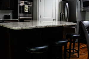 Kitchen featuring appliances with stainless steel finishes, dark wood-style floors, a kitchen island, and dark cabinetry