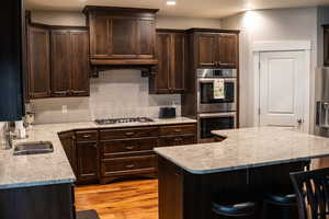 Kitchen with appliances with stainless steel finishes, a sink, decorative backsplash, a kitchen bar, and dark brown cabinets