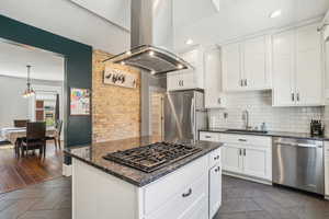 Kitchen with view of original brick wall, island range hood, a sink, tasteful backsplash, and white cabinets