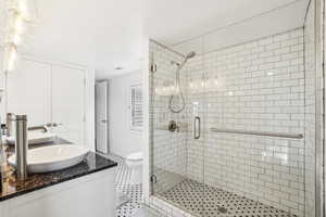 Bathroom with a luxury glass shower, vanity, toilet, tile patterned floors, and baseboards