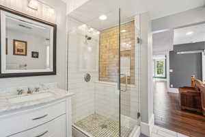 Full bathroom featuring a glass shower stall, vanity, baseboards, wood finished floors, and recessed lighting