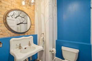 1/2 Bath with toilet, original brick wall, and a sink