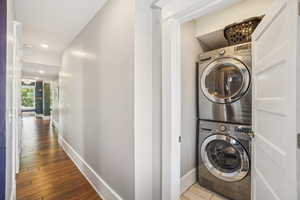 Washroom with stacked washing machine and dryer, baseboards, wood finished floors, and recessed lighting