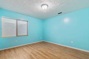 Unfurnished room with wood finished floors, baseboards, and a textured ceiling