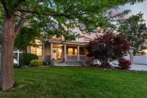 View of property hidden behind natural elements with a porch, a front lawn, an attached garage, stone siding, and stucco siding