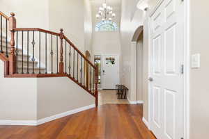Foyer featuring wood finished floors, stairway, arched walkways, a chandelier, and baseboards
