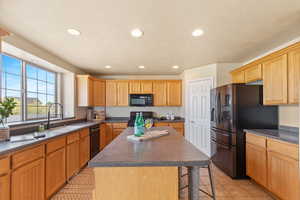 Kitchen featuring black appliances, dark countertops, a sink, a breakfast bar area, and recessed lighting